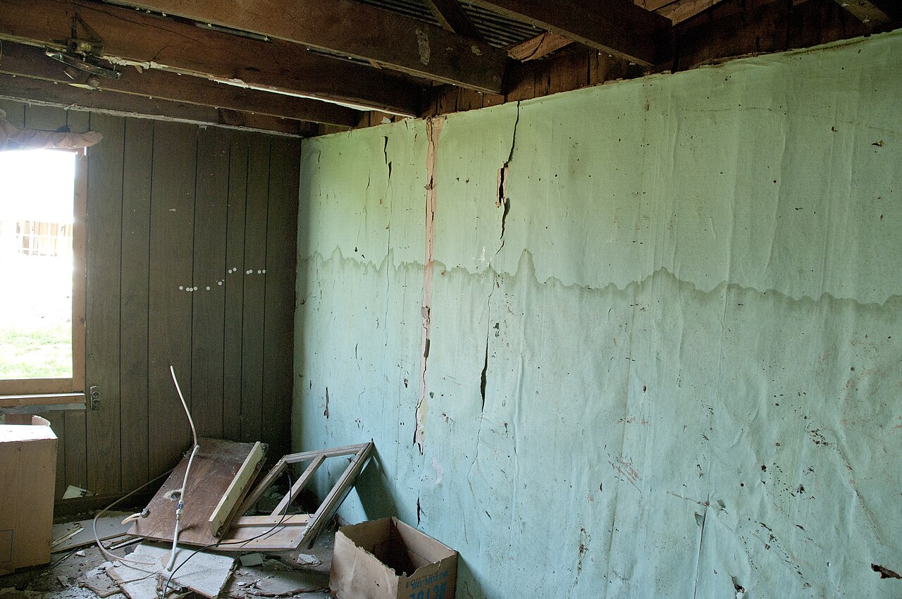 Water damage restoration technician assessing interior water damage from leaking pipe